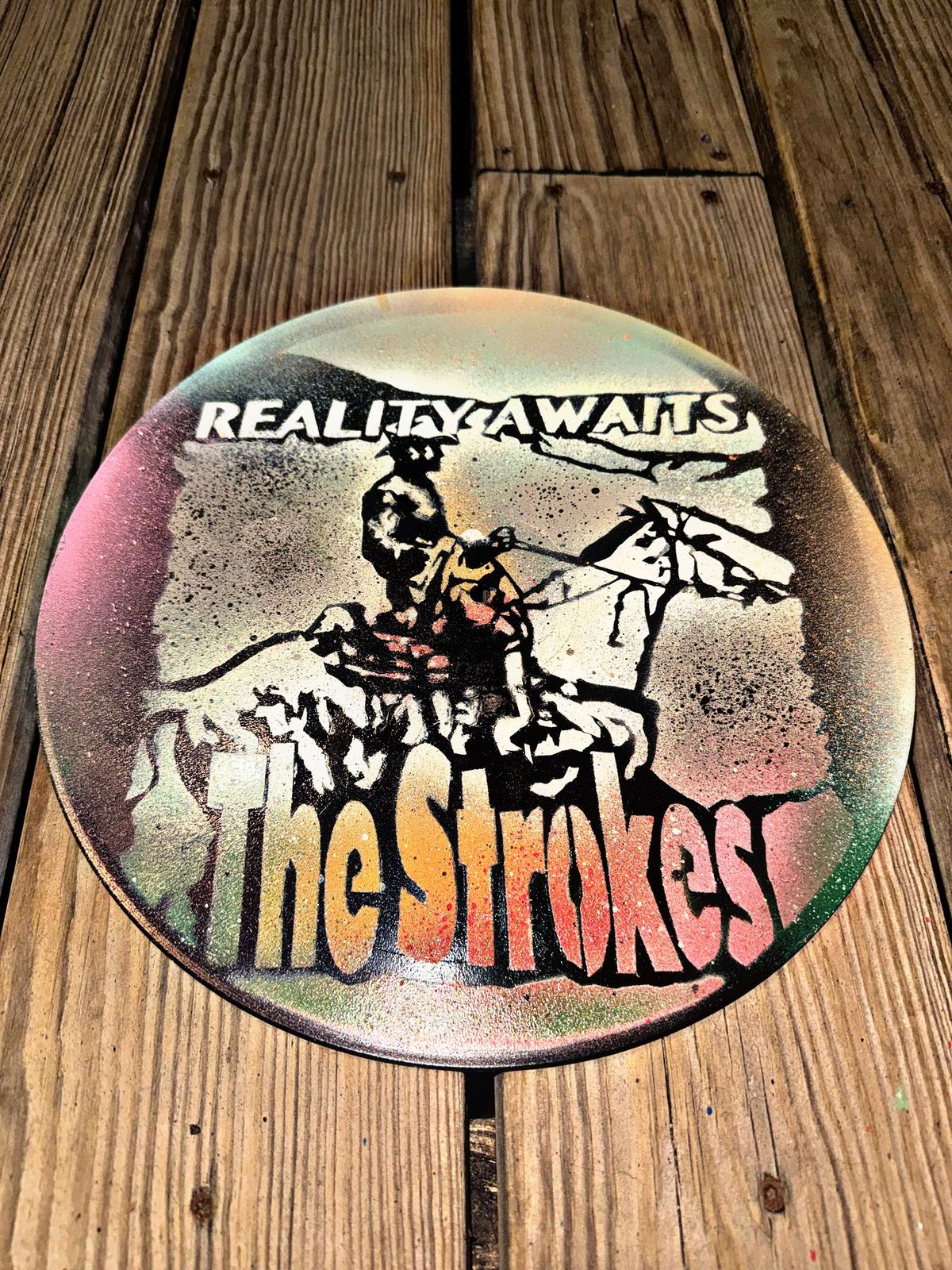 The Strokes lettering and a rider on horseback stenciled on a vinyl record by Andres Gallardo