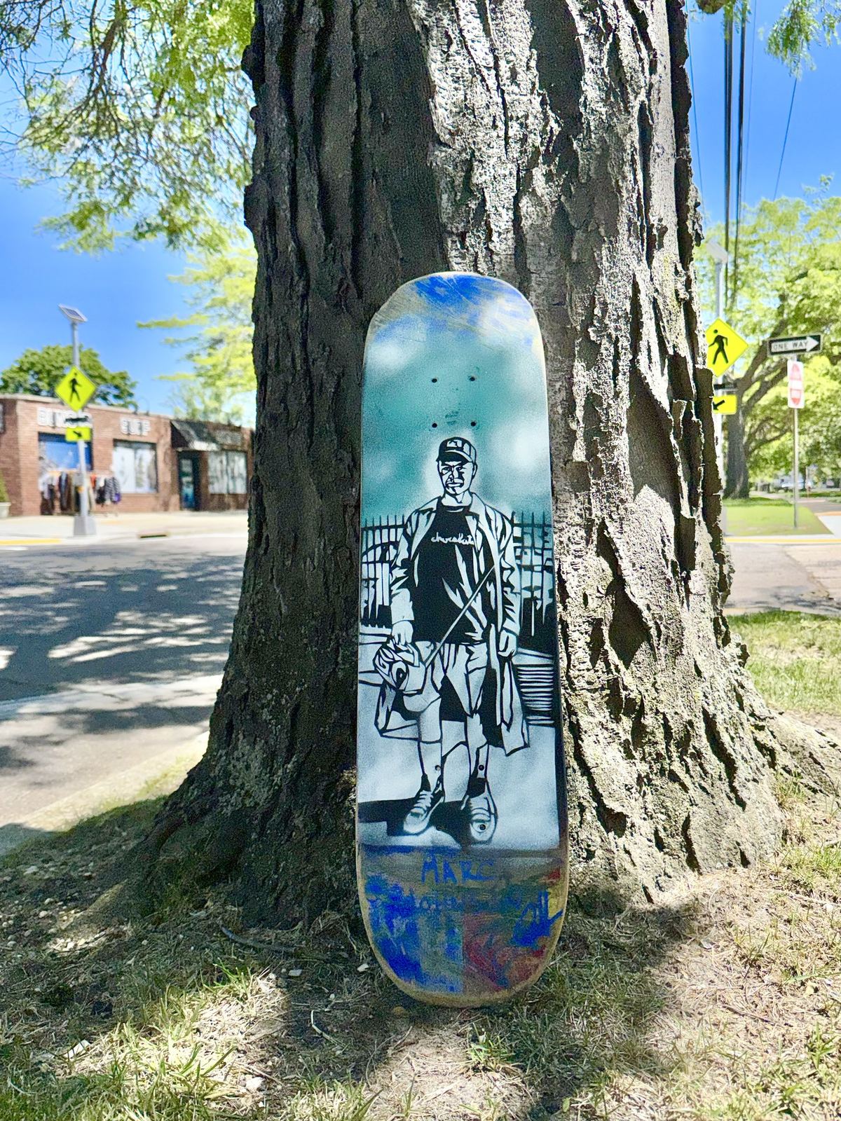 A stencil-painted skateboard leaning against a tree, by Andres Gallardo