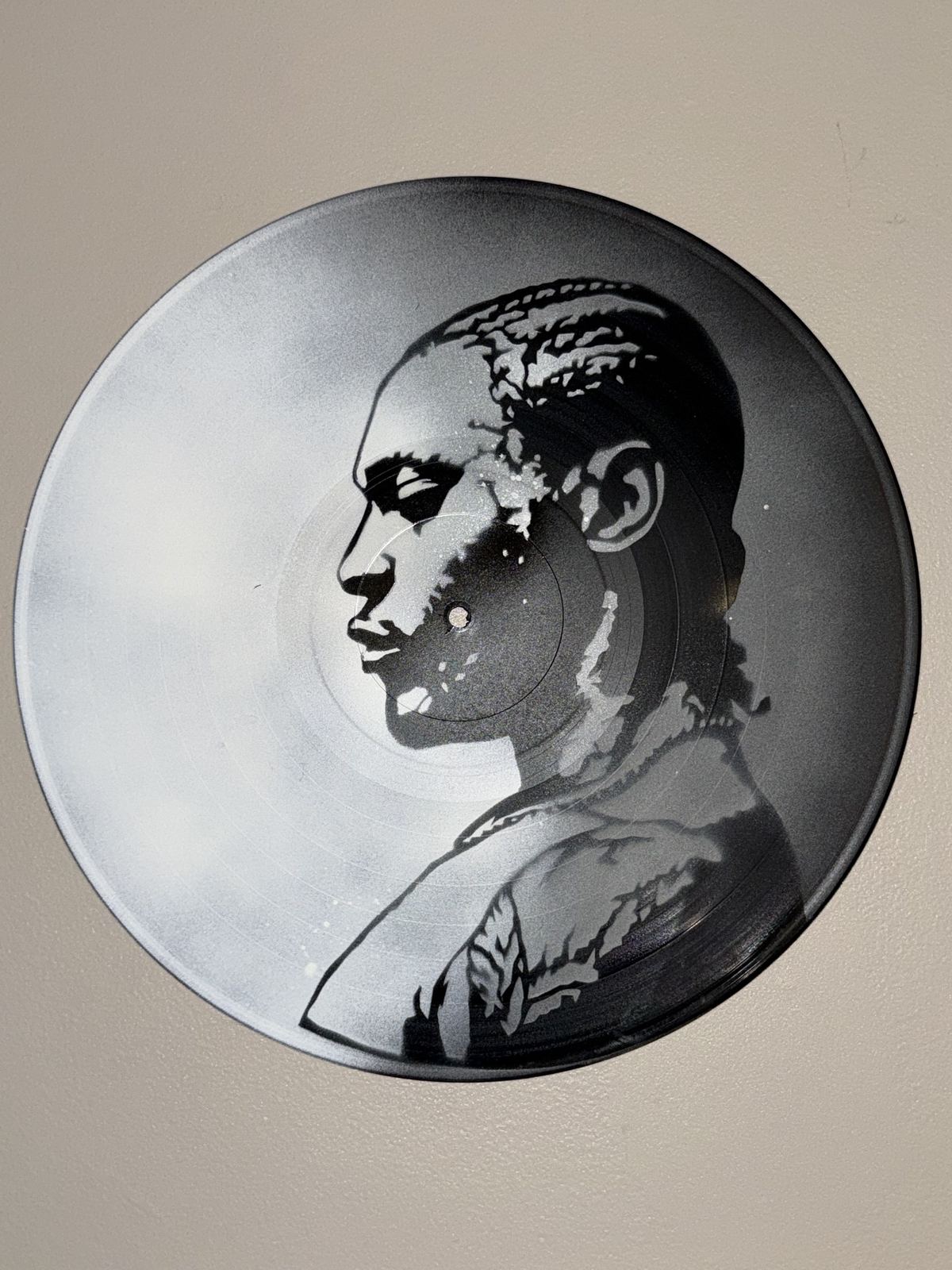 Black and white stencil portrait of a man in profile on a vinyl record by Andres Gallardo