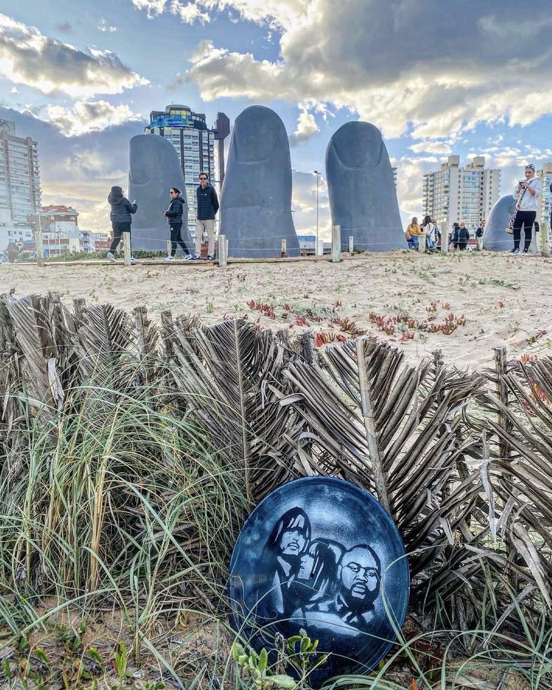 A GEM Movement record piece in the dune grass beside the hand sculpture at Punta del Este, Uruguay