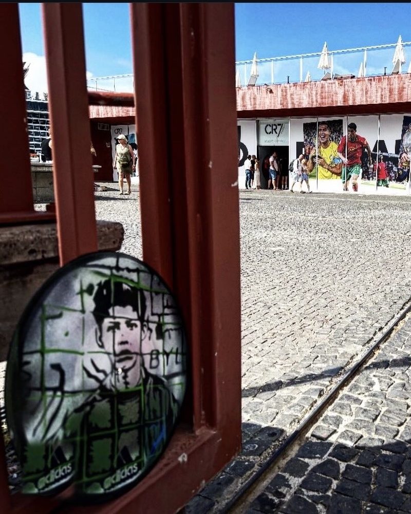 A GEM Movement record piece of a young Cristiano Ronaldo in a red doorframe across from a CR7 mural in Funchal, Portugal